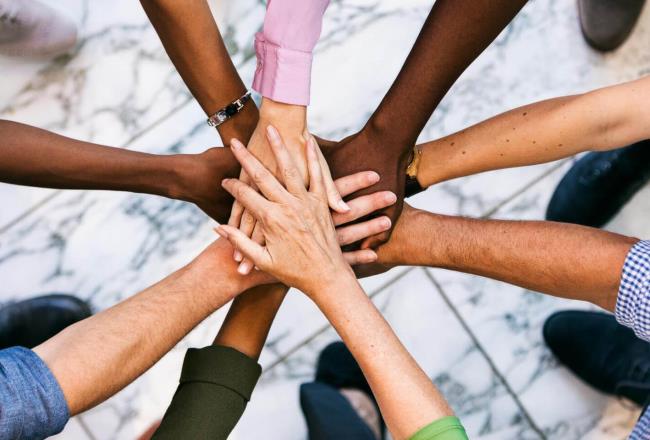 Gruppe von Menschen, die im Kreis aufgestellt ihre Hände übereinander legen.