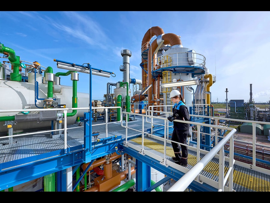Employee standing outside a factory, surrounded by pipes and silos.