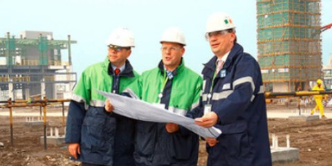 Drei Bauarbeiter mit Schutzhelmen inspizieren Baupläne auf einer Baustelle.