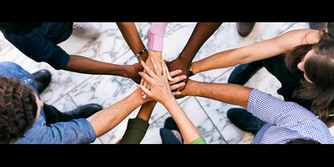 Gruppe von Menschen, die im Kreis aufgestellt ihre Hände übereinander legen.