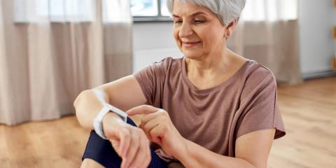An elderly woman sits in her apartment and operates her smartwatch.