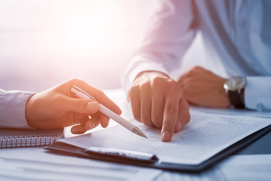 Two people working on a document, one pointing with a pen and the other with their pointer finger.